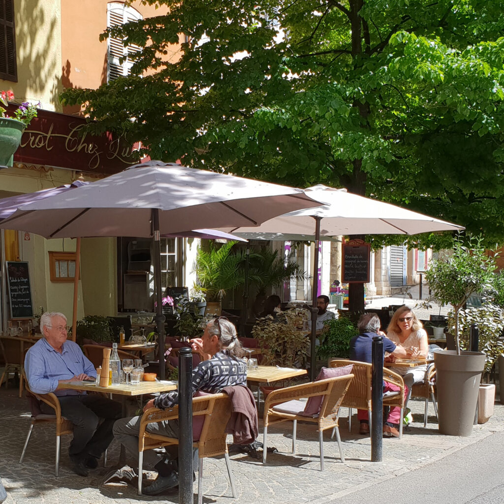 De Hoofdstraat in Lorgues met historische panden, terrasjes met parasols en mensen die buiten zitten.