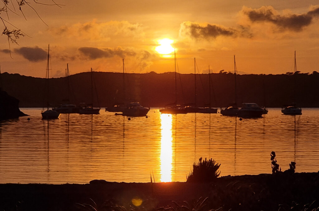 Sonnenuntergang in der Bucht von Port-Cros mit Segelbooten und dem Spiegelbild ihrer Masten im welligen Wasser.