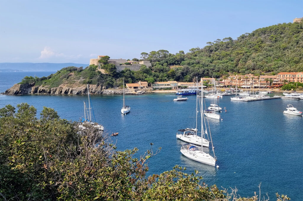 Panoramablick von einem Hügel auf die Bucht von Port-Cros mit vor Anker liegenden Segelbooten, Fort du Moulin, die Hafengebäude darunter Hostellerie Provençale und das Meer in Richtung der Berge bei Hyères.