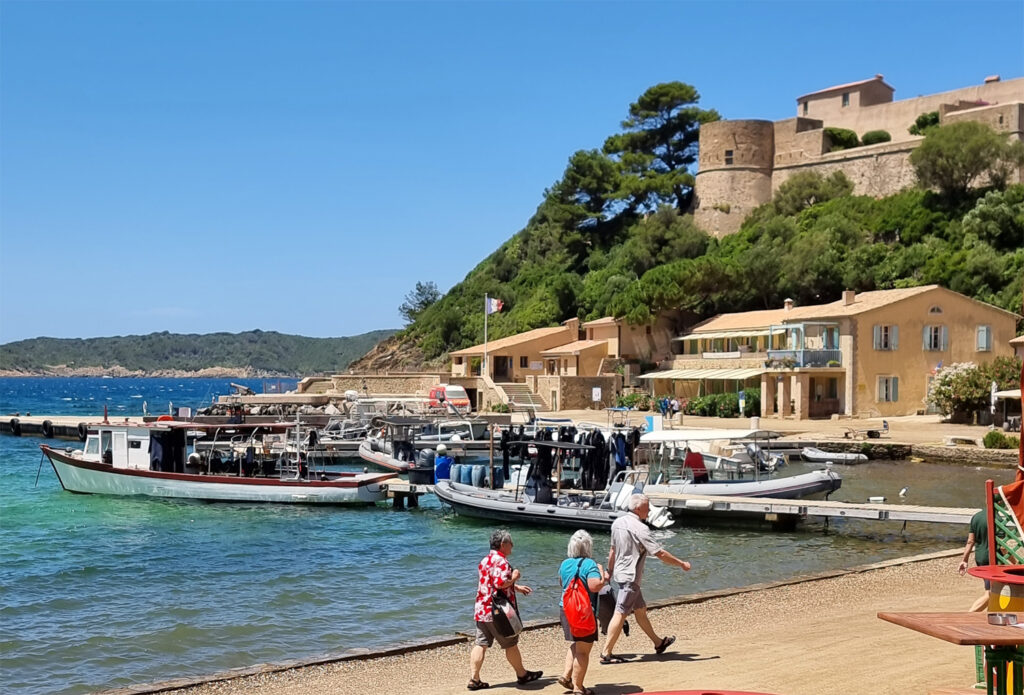 Hafen von Port-Cros mit den beiden Booten der Tauchschule Sun Port Cros, dem Hafenmeistergebäude mit französischer Flagge und dem Fort du Moulin im Hintergrund.