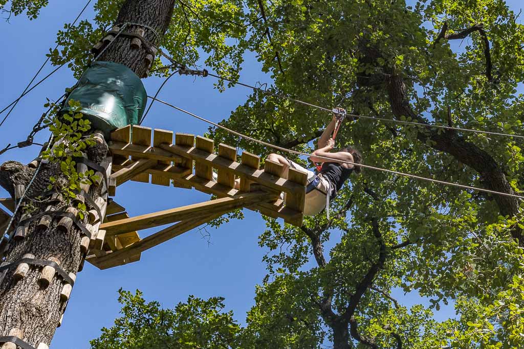 Bezoekers die hoog in de bomen over een klimparcours bewegen in Les Rochers de Maguelone bij Montpellier, gezien vanuit een lage hoek.