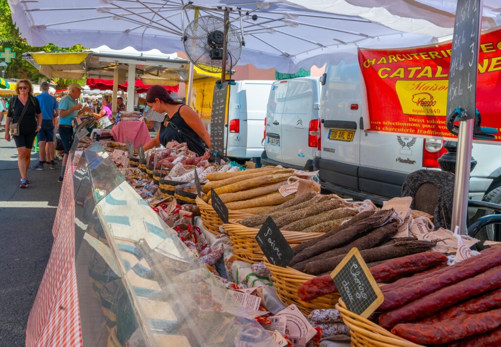 Kraampjes op de markt op de Place aux Herbes in Uzès, met op de voorgrond een stand vol verschillende soorten gedroogde charcuterie.