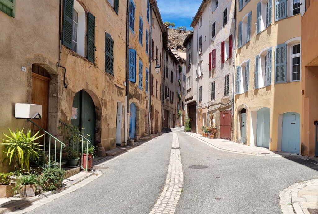Smalle, spits toelopende straat in Cotignac met hoge historische panden en de imposante rotsen die boven de huizen uitrijzen