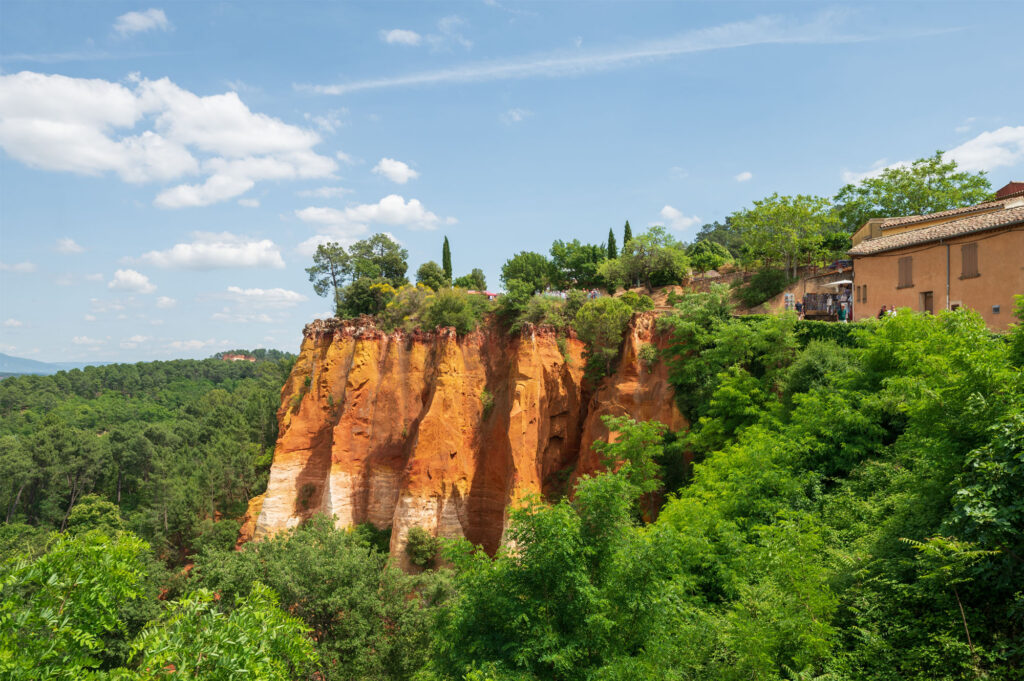 Okerrode rotspartijen van Roussillon vanaf de brug met veel groen en blauwe lucht