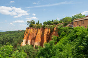Okerrode rotspartijen van Roussillon vanaf de brug met veel groen en blauwe lucht