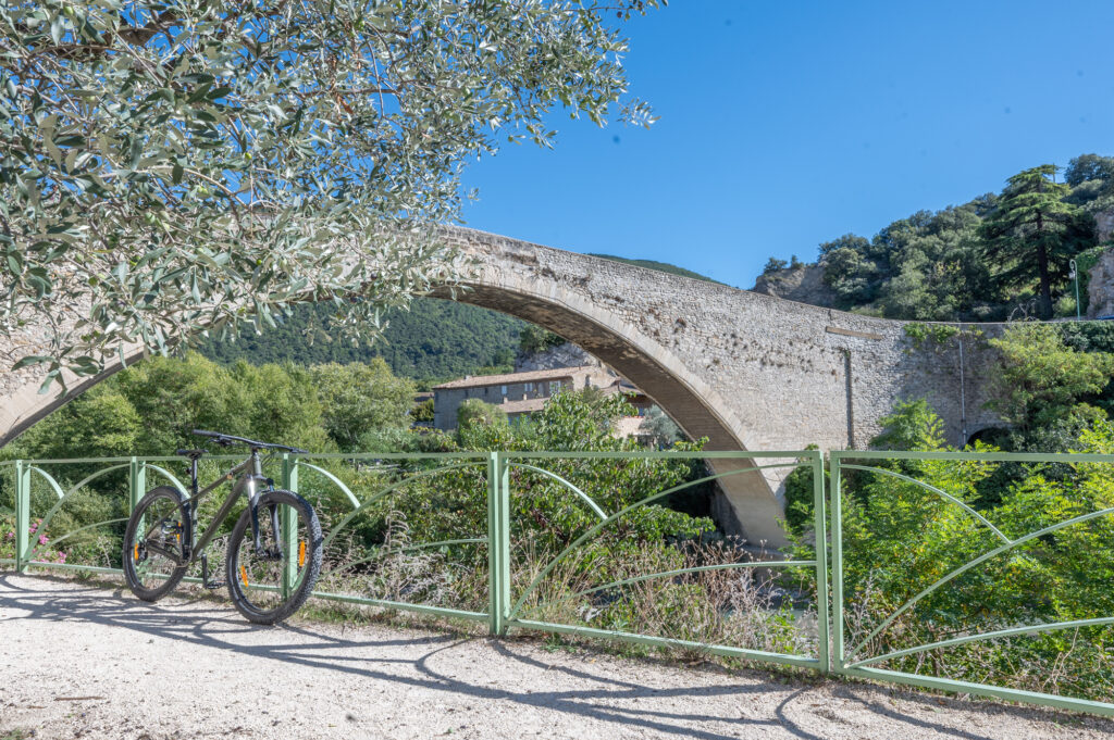 Mountainbike geparkeerd tegen een railing bij de rivier de Eygues in Nyons, een populaire bestemming voor fietsliefhebbers en outdoor-avonturen in de Provence.