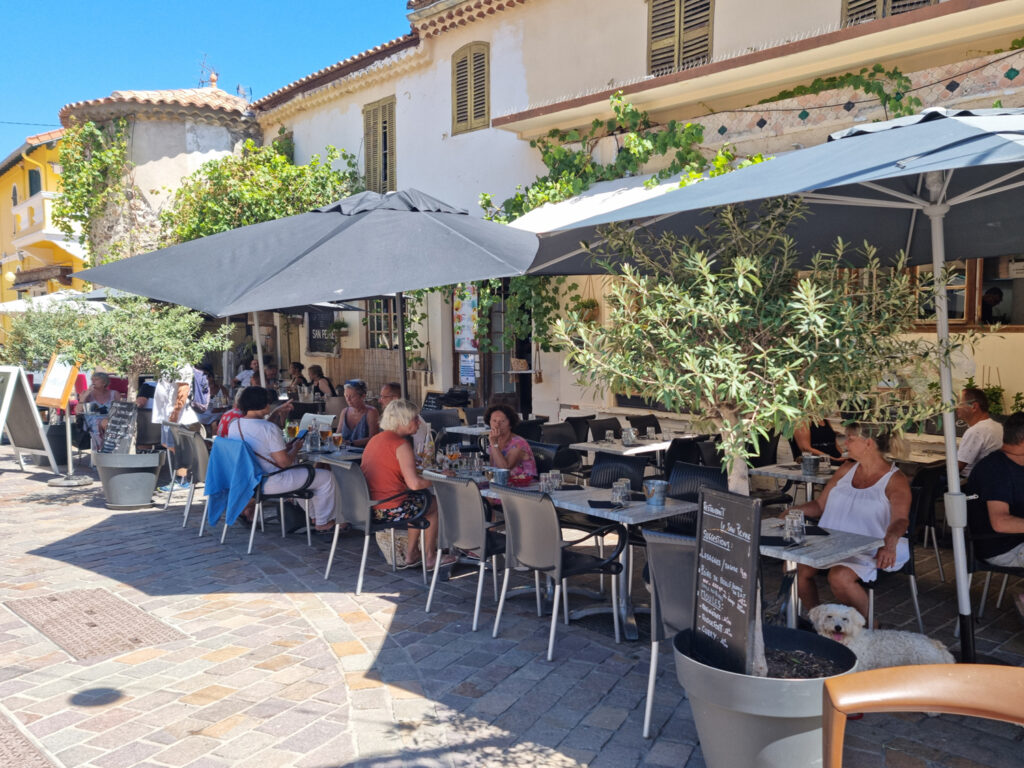 Terrasses agréables dans le vieux centre de La Napoule, entourées d'arbres ombragés et de bâtiments historiques colorés.