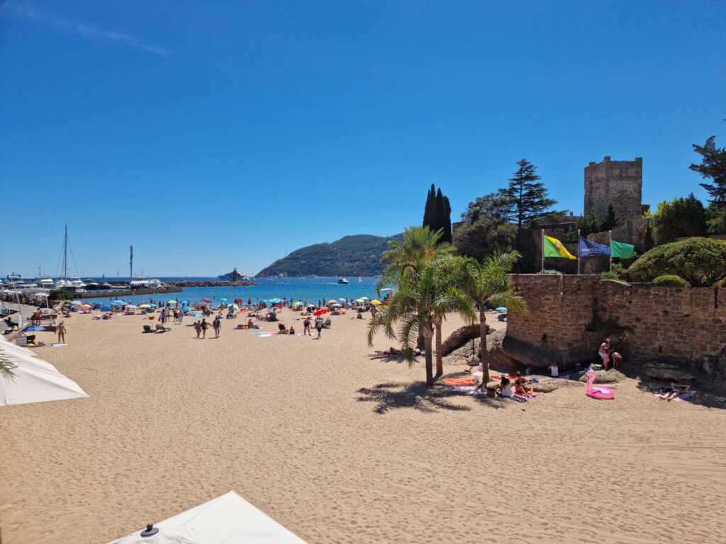 Plage de sable de La Napoule avec une mer bleu clair et des formations rocheuses en arrière-plan.