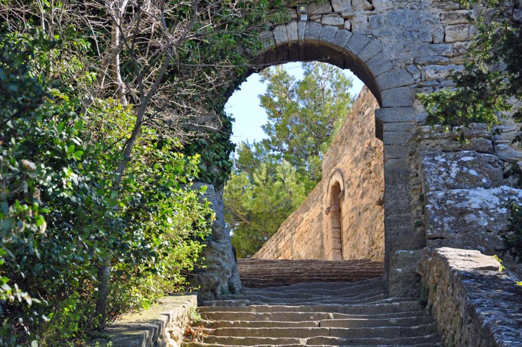Een historische stenen trap in Bonnieux, omgeven door oude muren en een poort die leidt naar een verborgen kerk.