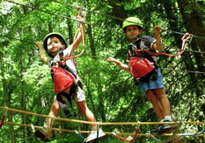 Twee jongens met helm en veiligheidstuigje op een loopbrug in een klimpark.