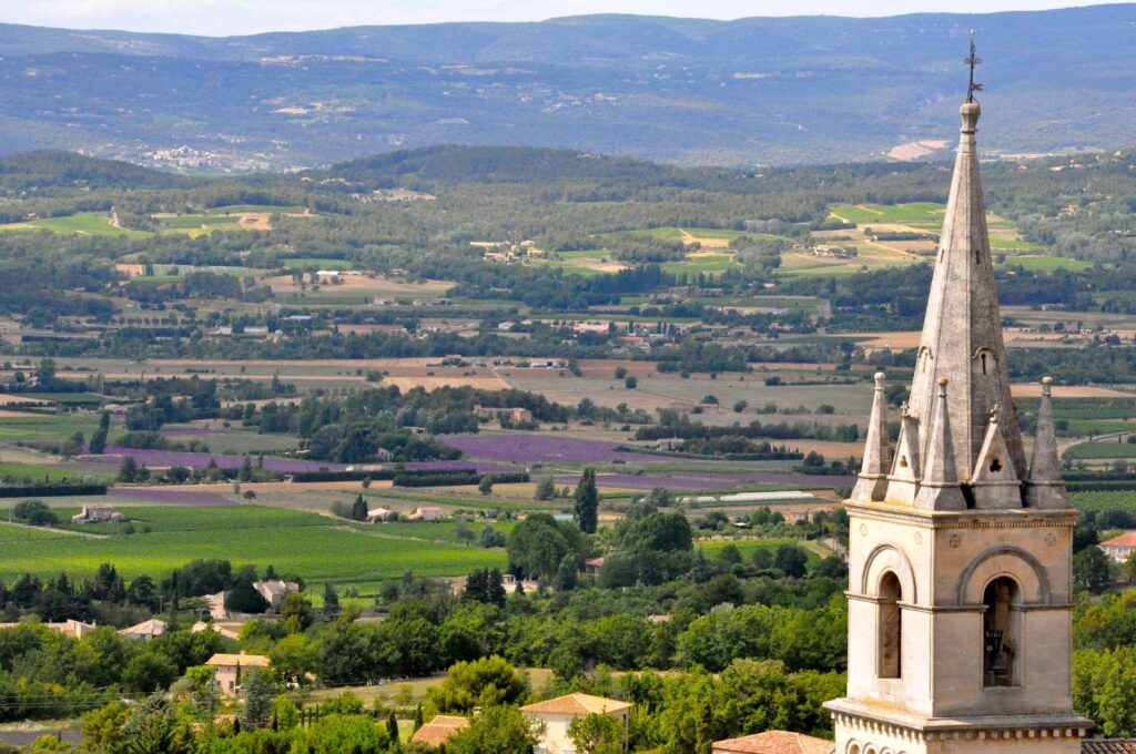 De kerktoren van Bonnieux met op de achtergrond een uitgestrekte vallei en paarse lavendelvelden.