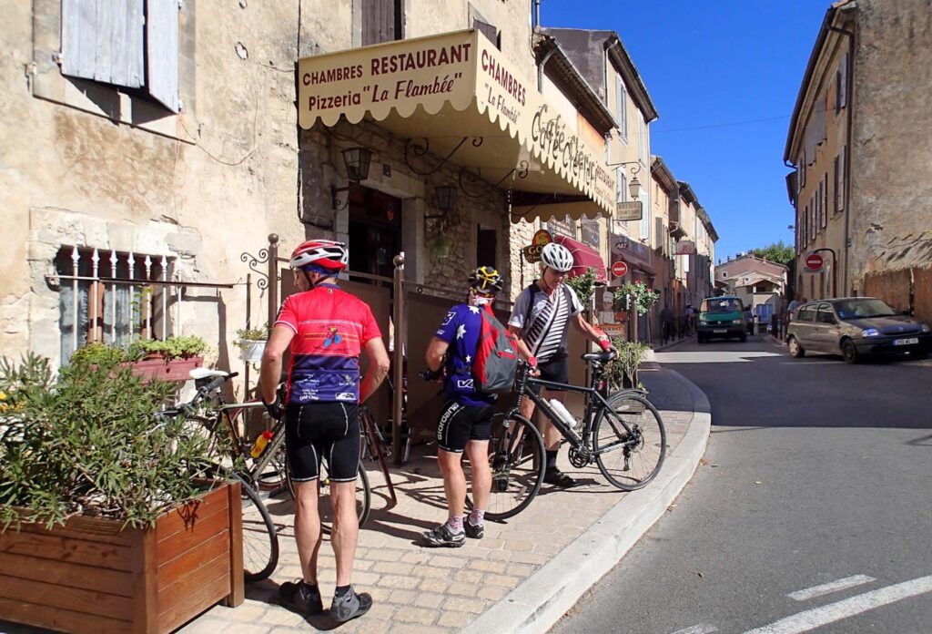 Een groep racefietsers neemt een pauze in het schilderachtige dorp Bonnieux, met hun fietsen geparkeerd tegen een oude stenen muur.