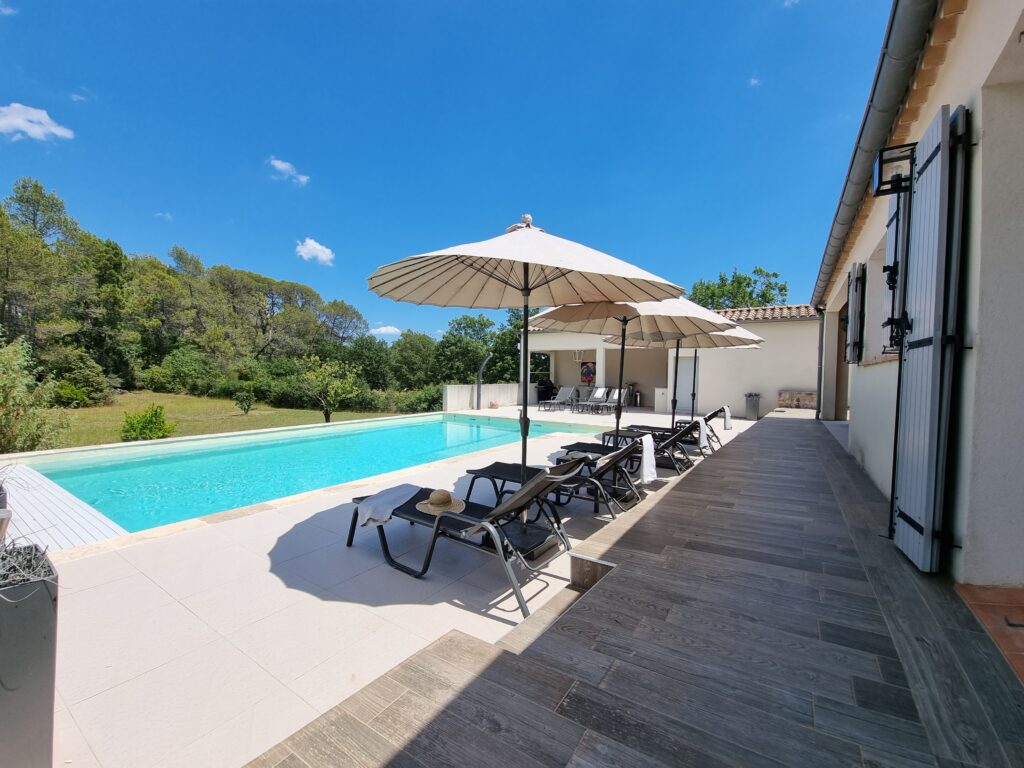 Zwembad van Villa La Gourmandise met brede traptreden, ligbedden met parasols en de villa op de achtergrond