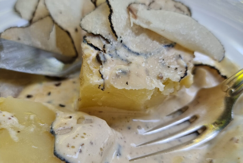 Ingezoomd gerecht bij Chez Bruno in Lorgues met plakjes verse truffel op romige aardappel, met vork en mes in beeld.