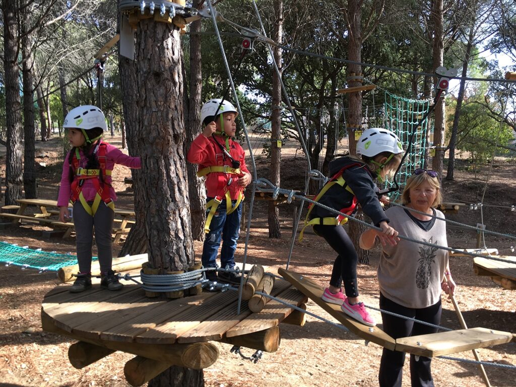 Kinderen met helm en veiligheidstuigje op een laag parcours in klimpark Aventure Famille in Sainte-Maxime, bij een platform rond een boomstam.