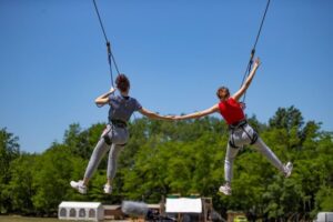 Twee meisjes die tegelijk van een zipline afglijden in Accroche Aventure, terwijl ze elkaars hand vasthouden.