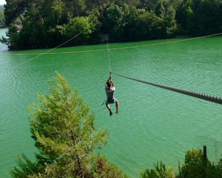 Bezoeker met helm en veiligheidstuigje die met een zipline over het meer zweeft in klimpark O2 Aventure bij Carcassonne.