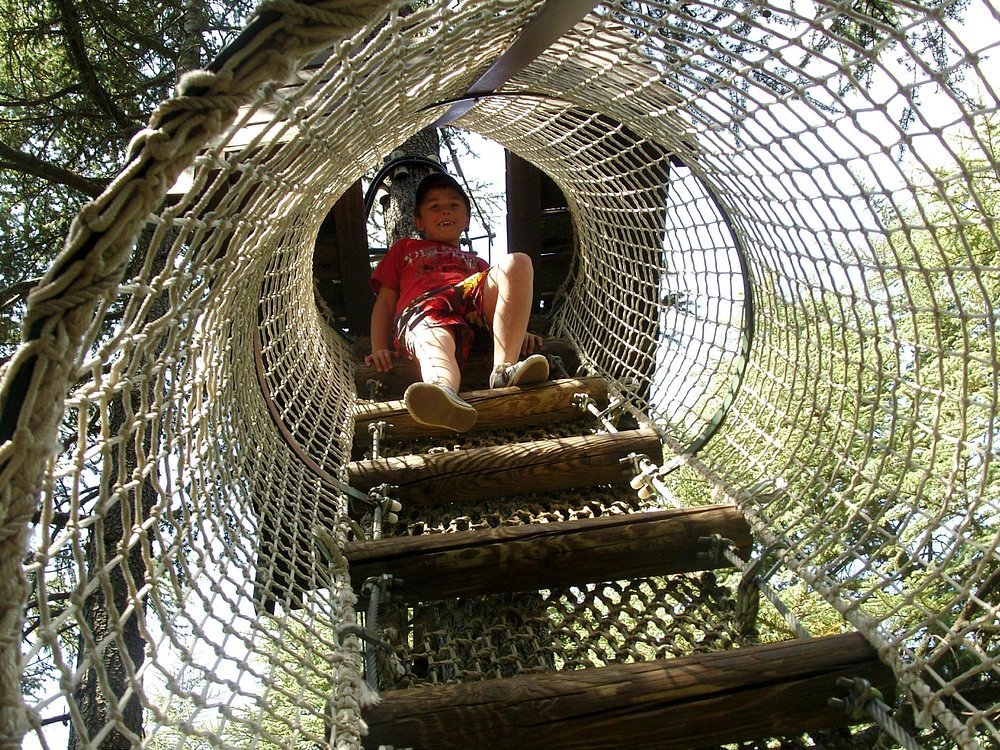 Bezoeker die over een loopbrug klimt in Aoubré L’Aventure Nature, met een veiligheidsnet rondom het parcours.