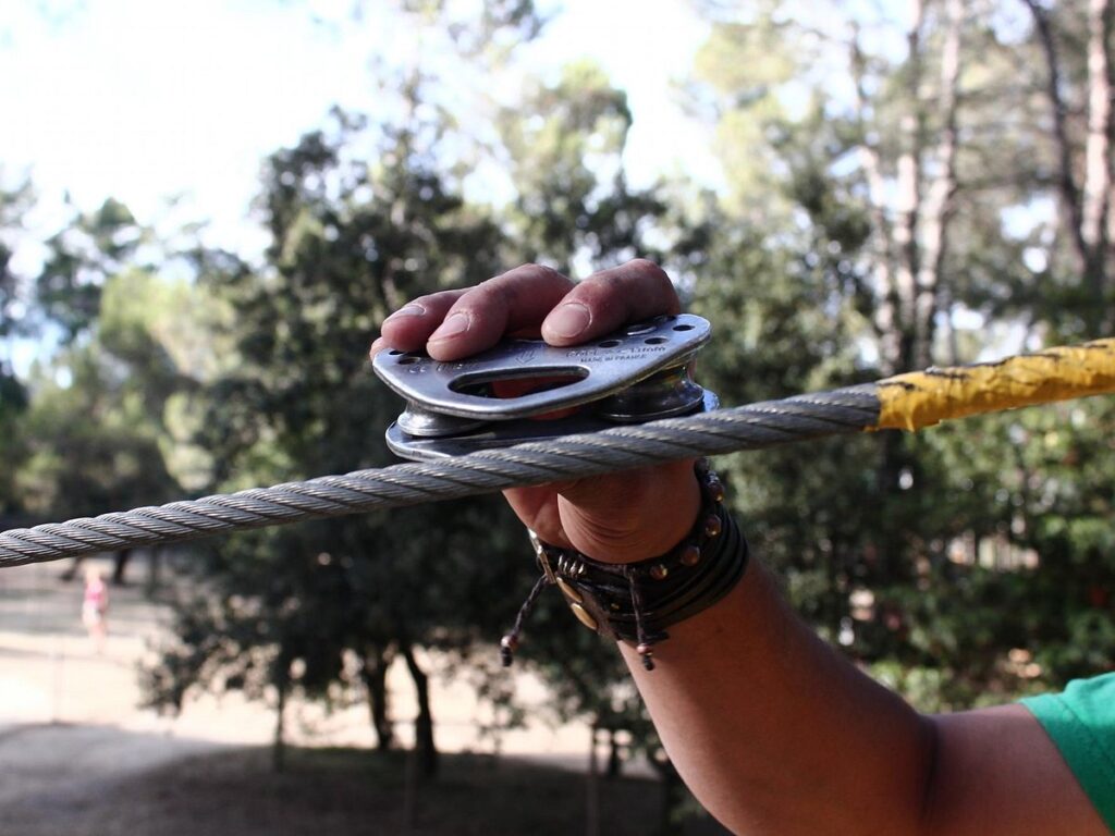 Hand met zekering aan kabel in klimpark O2 Aventure bij het meer van Carcassonne