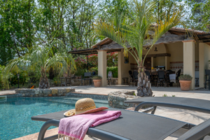 Straw hat and pink towel on a sun lounger by a private pool in Provence, surrounded by palm trees and Mediterranean light.