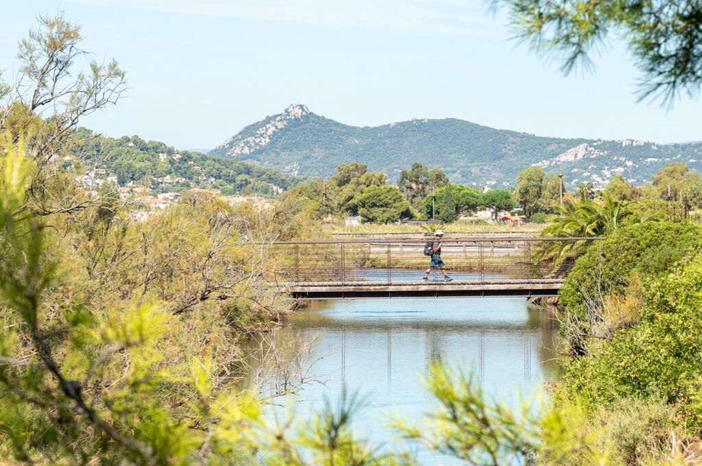 Houten voetbrug bij het natuurgebied van Hyères met uitzicht op het water en de bergen.