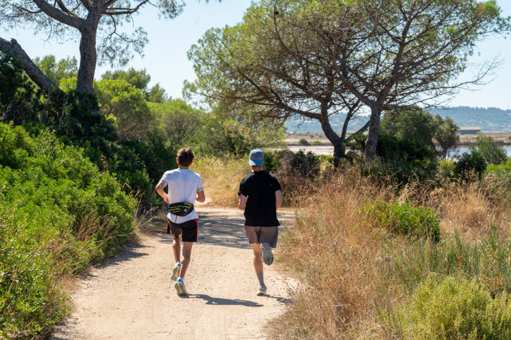 Zanderig wandel- en fietspad in Hyères met pijnbomen en twee hardlopers op de achtergrond