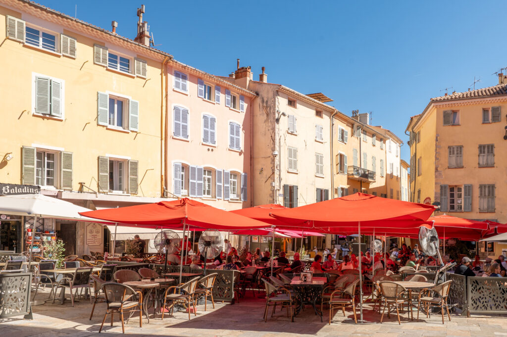 Zonnig plein in Hyères met rode parasols, terrassen en oude panden