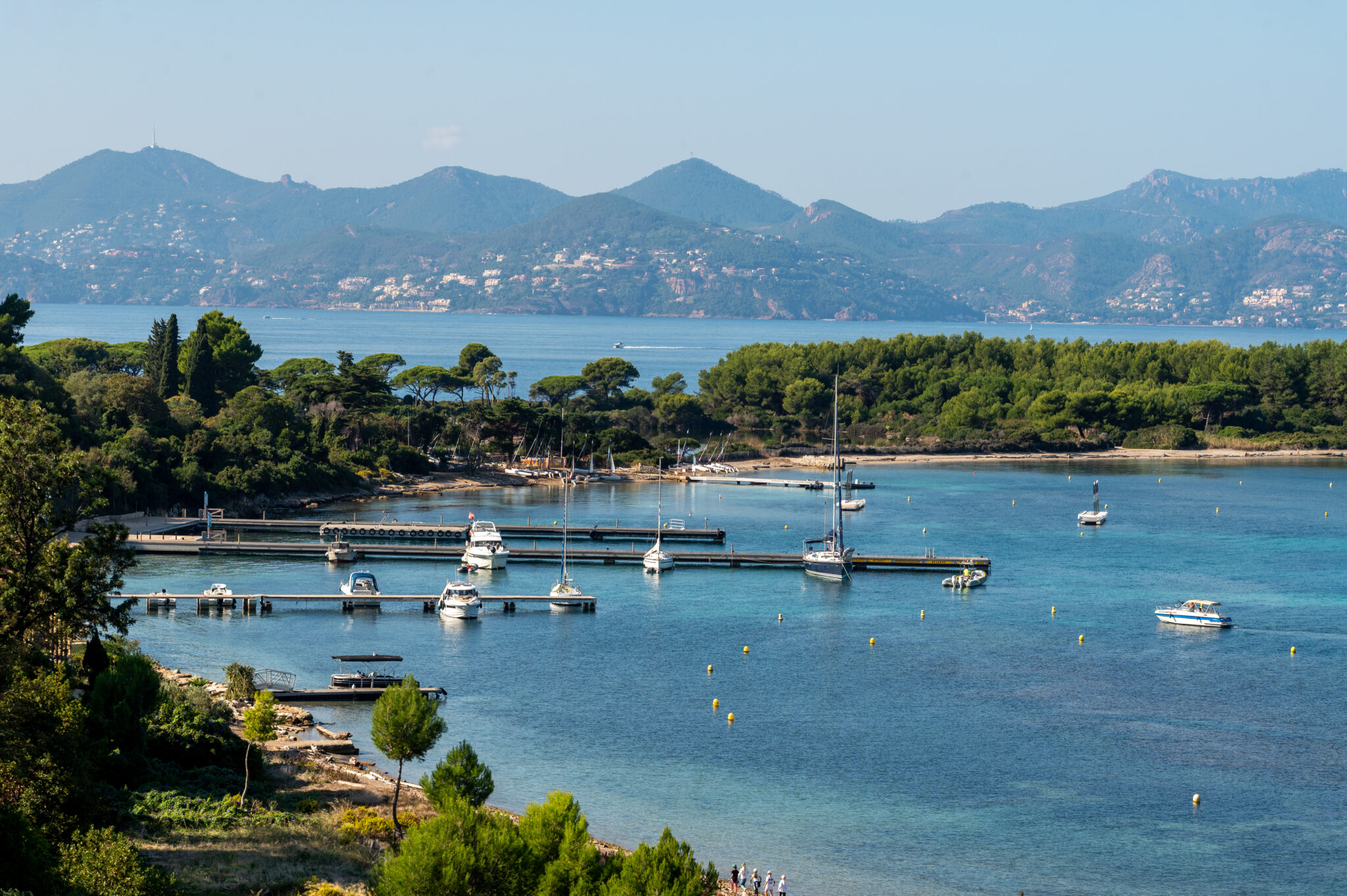 Uitzicht vanaf Île Sainte-Marguerite op de baai van Cannes met jachthaven, blauwe zee, groene eilandbossen en heuvels op de achtergrond.