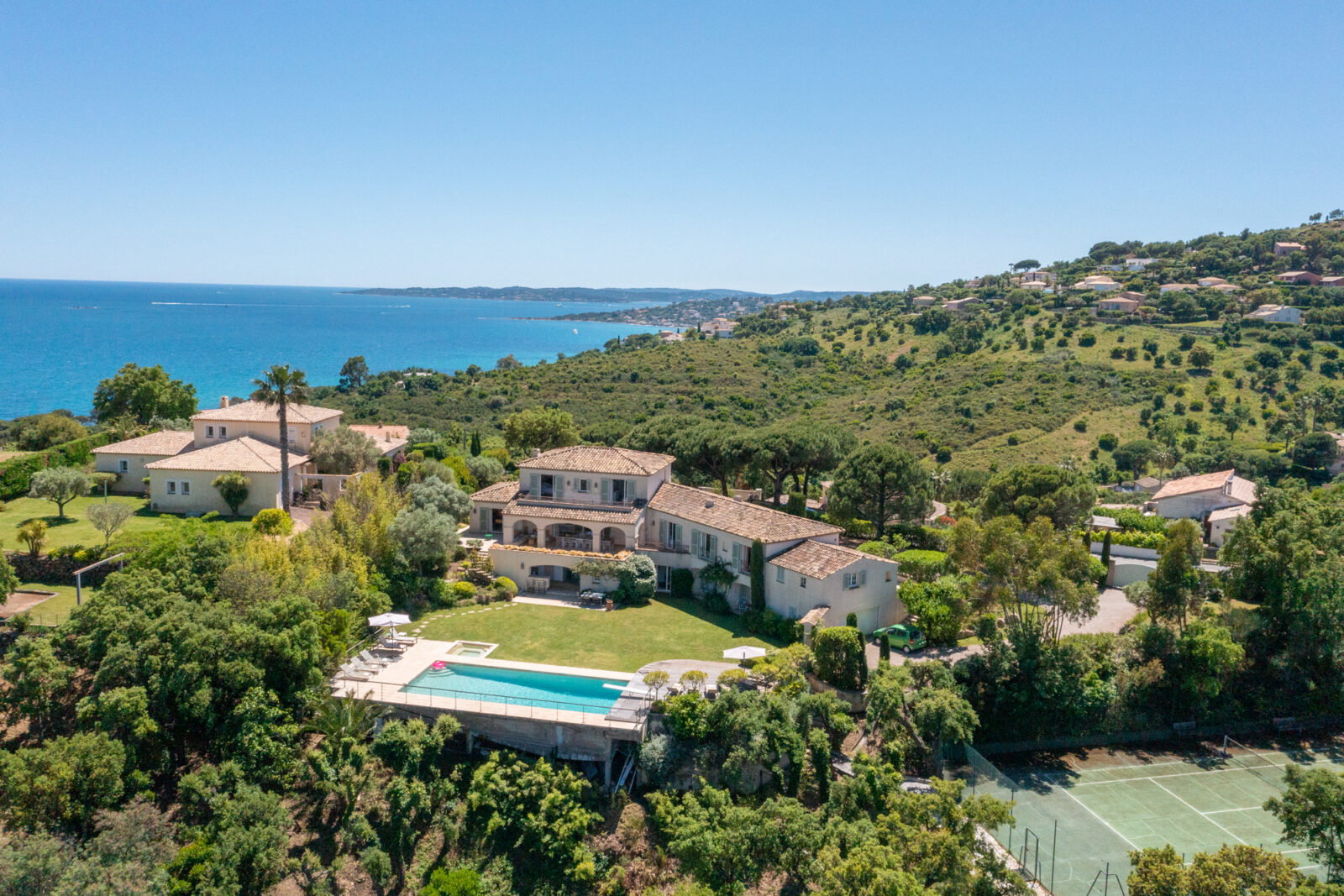 Luchtfoto van Villa Horizon in Sainte-Maxime met tennisbaan, zwembad met jacuzzi, groot gazon, tweelaagse villa en uitzicht op de azuurblauwe zee