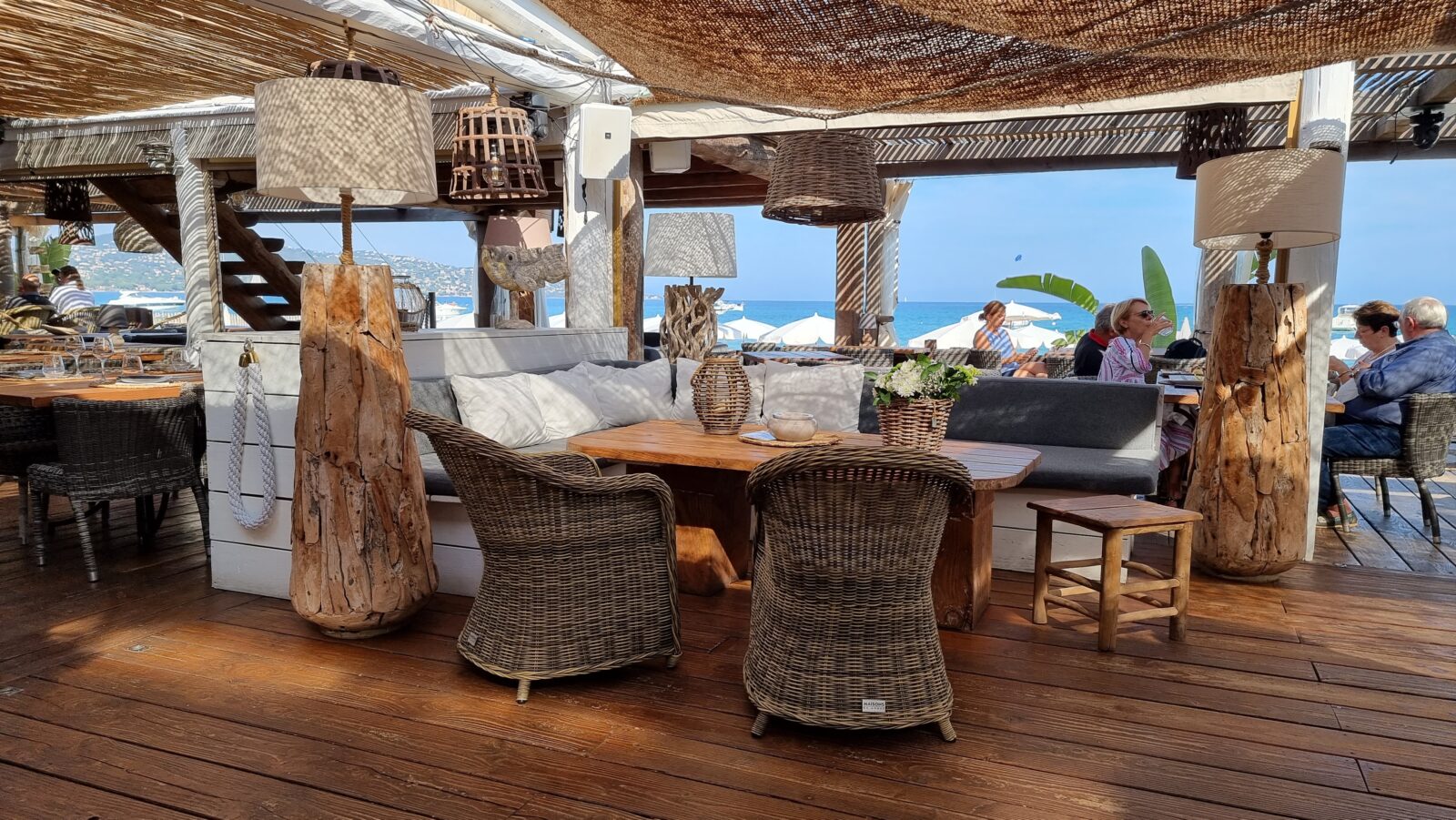 Interieur van Prao Beach in La Nartelle met houten details, gedekte tafels, doeken en uitzicht op parasols en zee