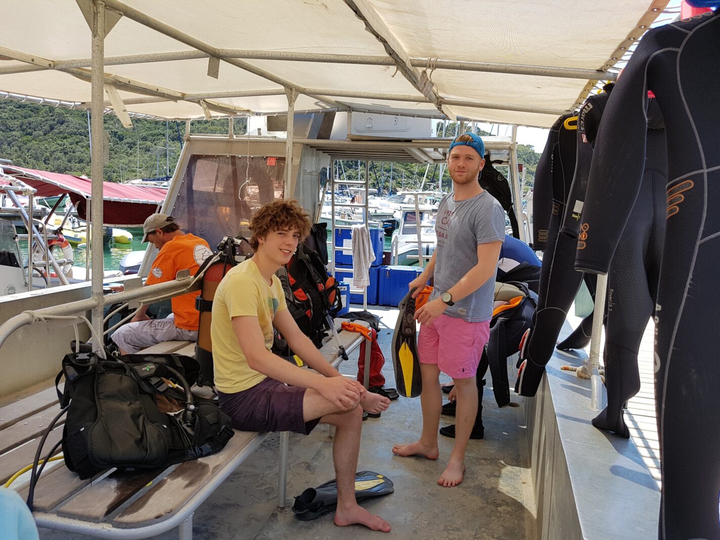 Duikboot van Sun Port-Cros met duikpakken en duikmateriaal, waarop twee jonge mannen glimlachend in de camera kijken.