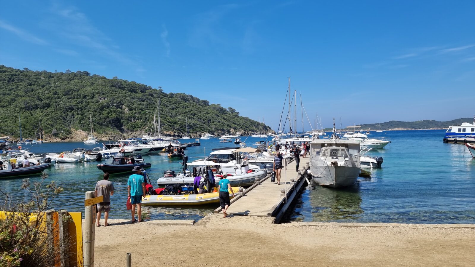 Zonnige foto vanaf de drijvende ponton in de haven van Port-Cros met boten, kleurrijke details, mensen en levendige drukte.